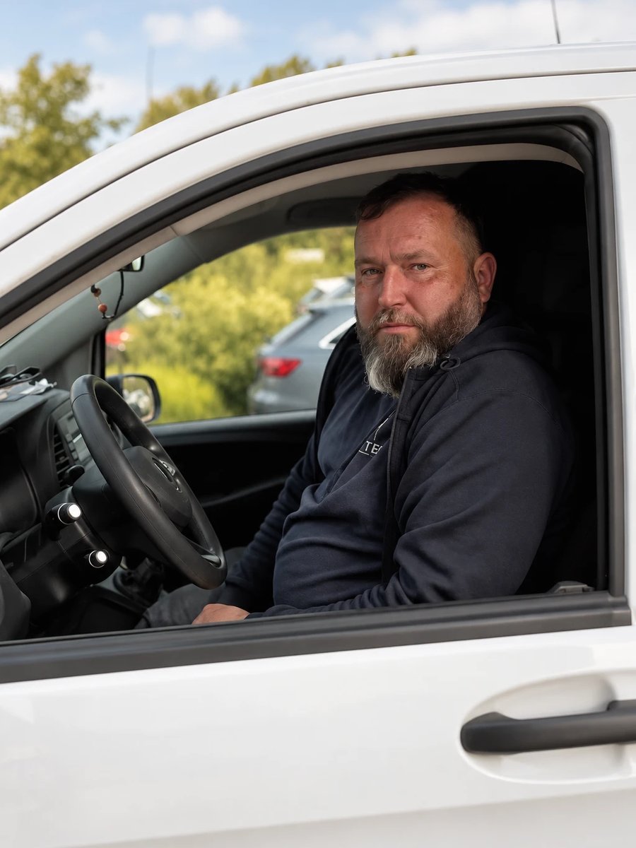 Ein Monteur sitzt am Steuer eines weissen Transporters und schaut aus dem Seitenfenster.