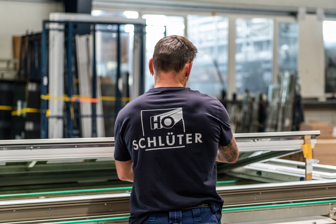 Ein Mitarbeiter im Schlüter-Shirt an einer Werkbank in der Fertigungshalle, von hinten.