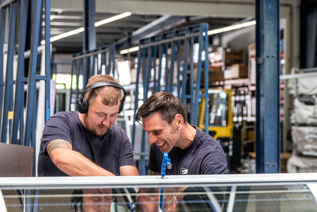 Zwei Kollegen arbeiten in der Fertigung gemeinsam an einem Fensterelement.