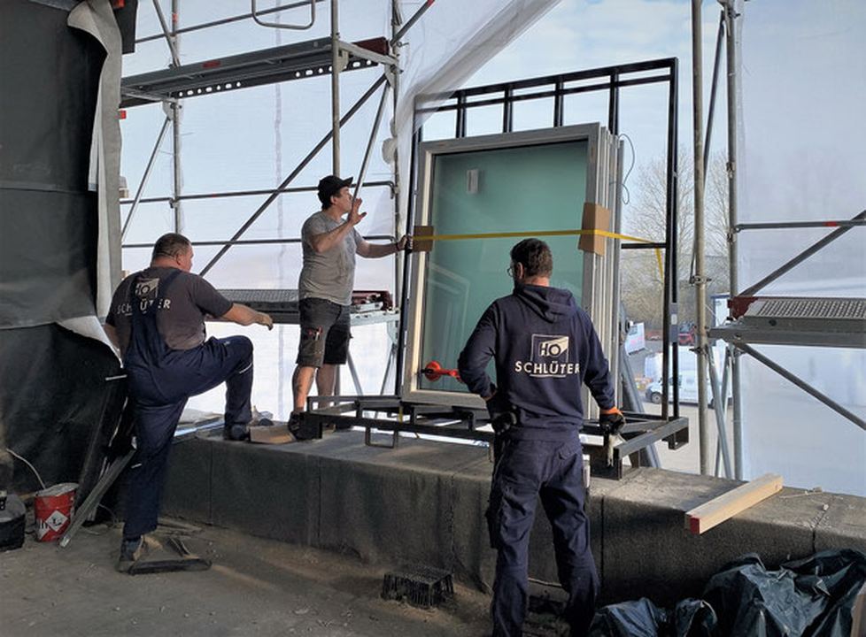 Drei Monteure setzen auf dem Gerüst ein großes Fassadenelement ein.